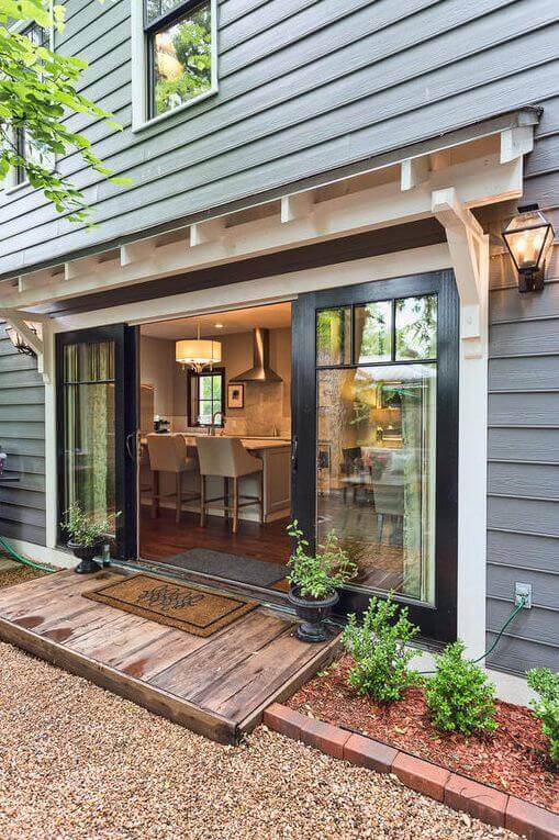 Welcoming entryway featuring double black-framed glass doors, natural wood planks, and a gravel path lined with low-maintenance plants.