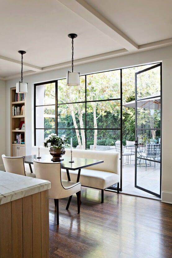 Modern dining area with large black-framed windows, polished hardwood flooring, and seamless access to a patio for outdoor dining.