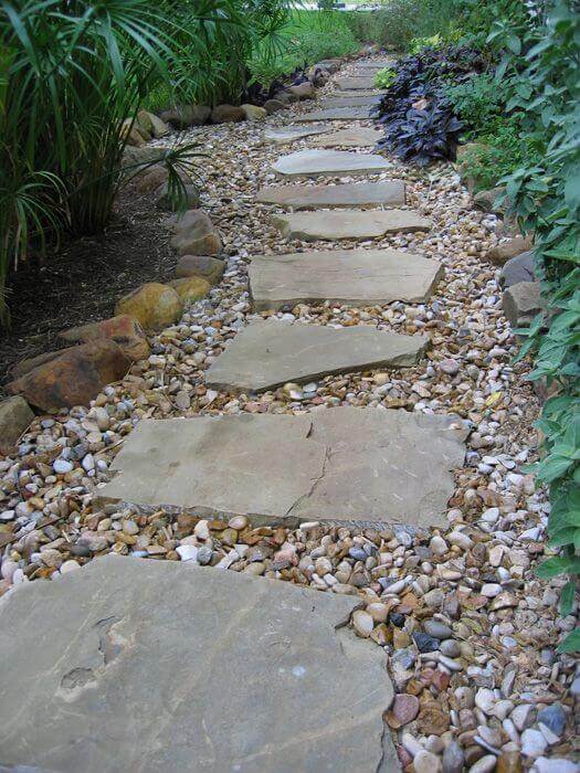 Flagstone pathway with irregular stepping stones, bordered by smooth river stones and lush green plants, creating a serene garden ambiance.