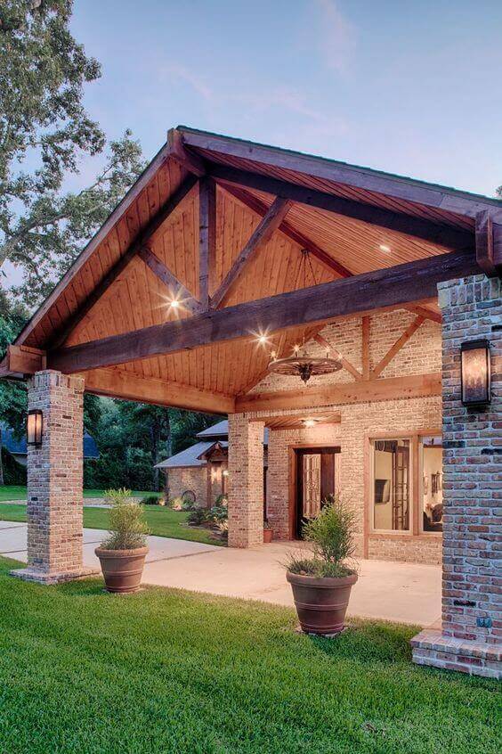 Covered pavilion entryway with wooden beams and steep roof, illuminated by integrated lighting for evening safety. Rustic and contemporary blend.