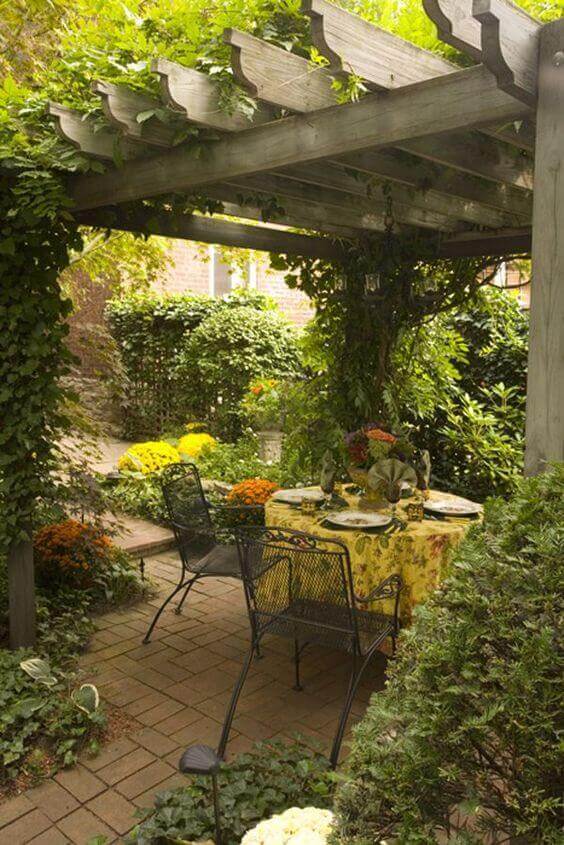 Cozy outdoor dining area under a wooden pergola, featuring a patterned tablecloth, black metal chairs, and vibrant flowers.