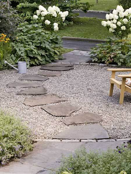 Flagstone and gravel walkway with flat slate stones, lush green plants, and blooming hydrangeas, creating a serene outdoor space.