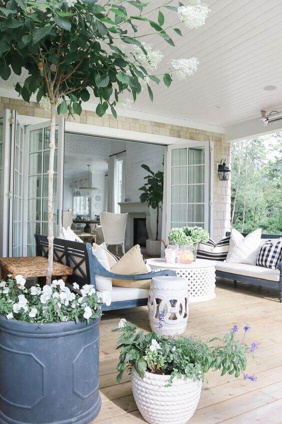 Back porch featuring a covered deck with wooden flooring, sectional sofa, decorative pillows, and floral planters for relaxation.