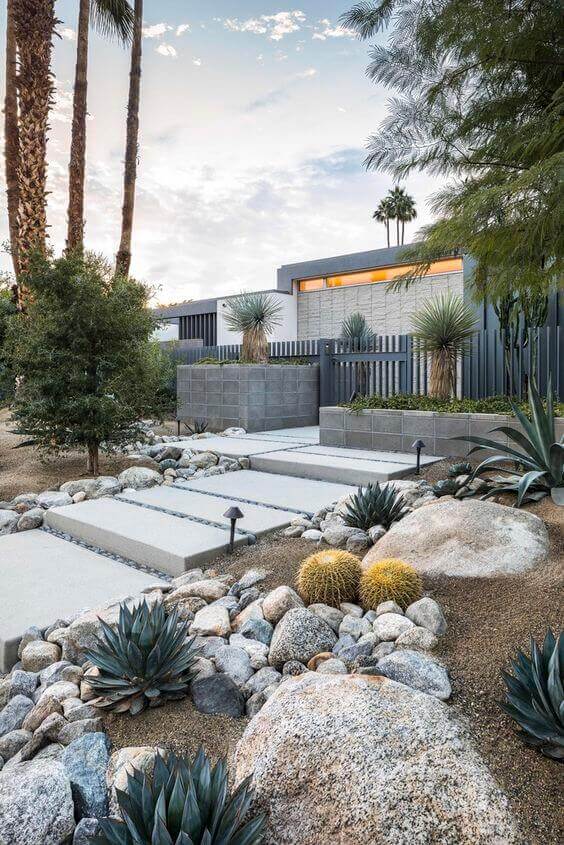Desert front yard features drought-resistant plants, a central concrete pathway, raised planters, and decorative gravel for low maintenance.