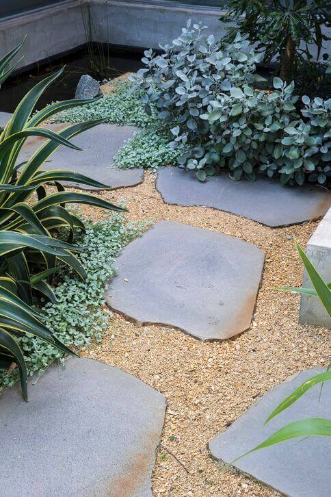 A flagstone pathway meanders through fine gravel, surrounded by lush foliage, creating a natural and modern landscape design.