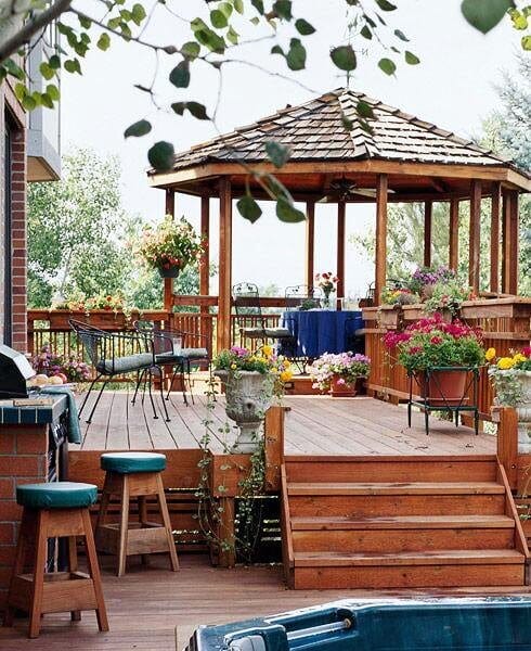 Gazebo with wooden posts and shingle roof, surrounded by a composite wood deck featuring potted plants and elevated steps for accessibility.