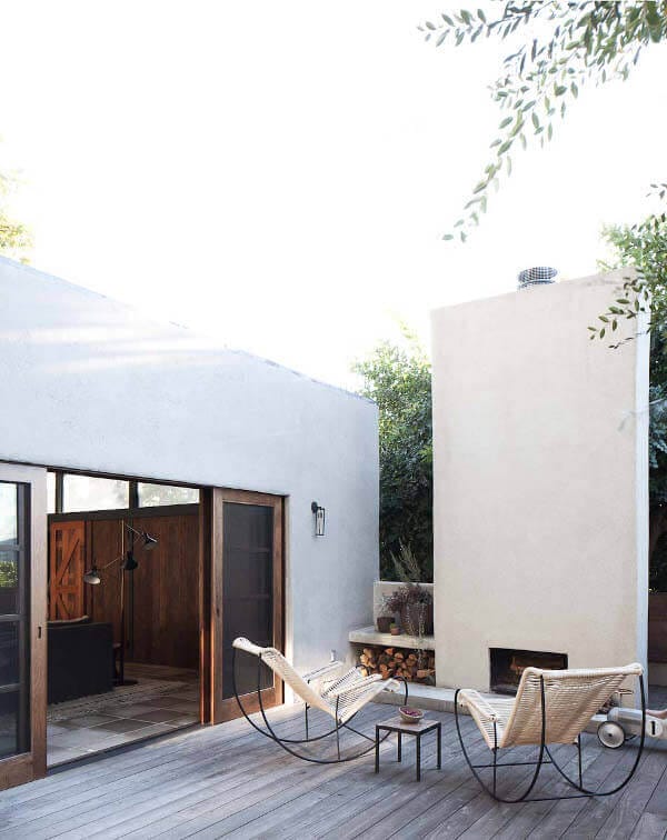 Contemporary outdoor space featuring a wooden deck, two curved lounge chairs, and a minimalist coffee table, surrounded by greenery.