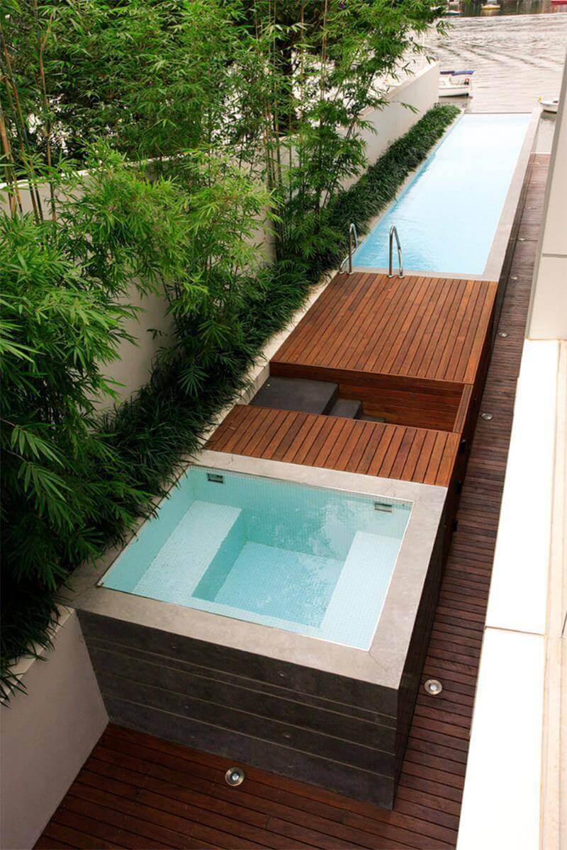 Modern wood deck design featuring a hot tub surrounded by natural wood decking and lush bamboo, complemented by a narrow lap pool.