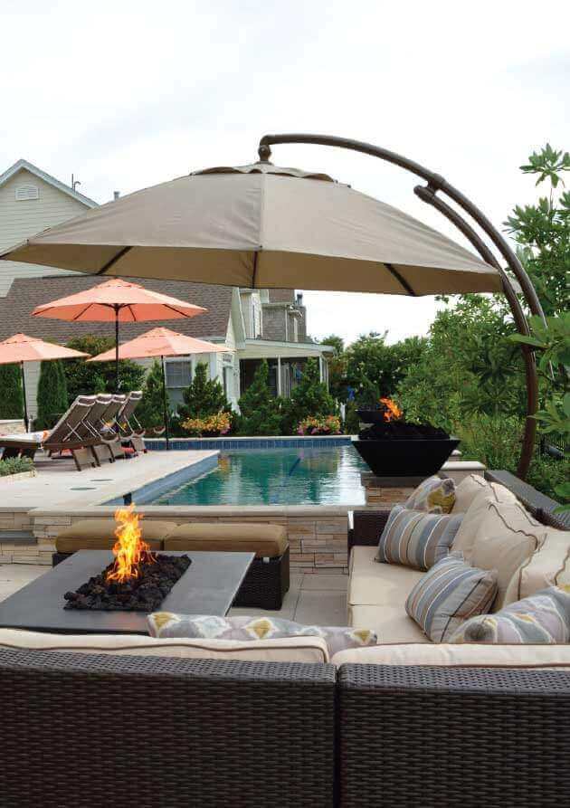 Outdoor swim spa area featuring a 15x30-foot pool, stone deck, lush landscaping, modern sectional sofa, and umbrella-shaded tables.