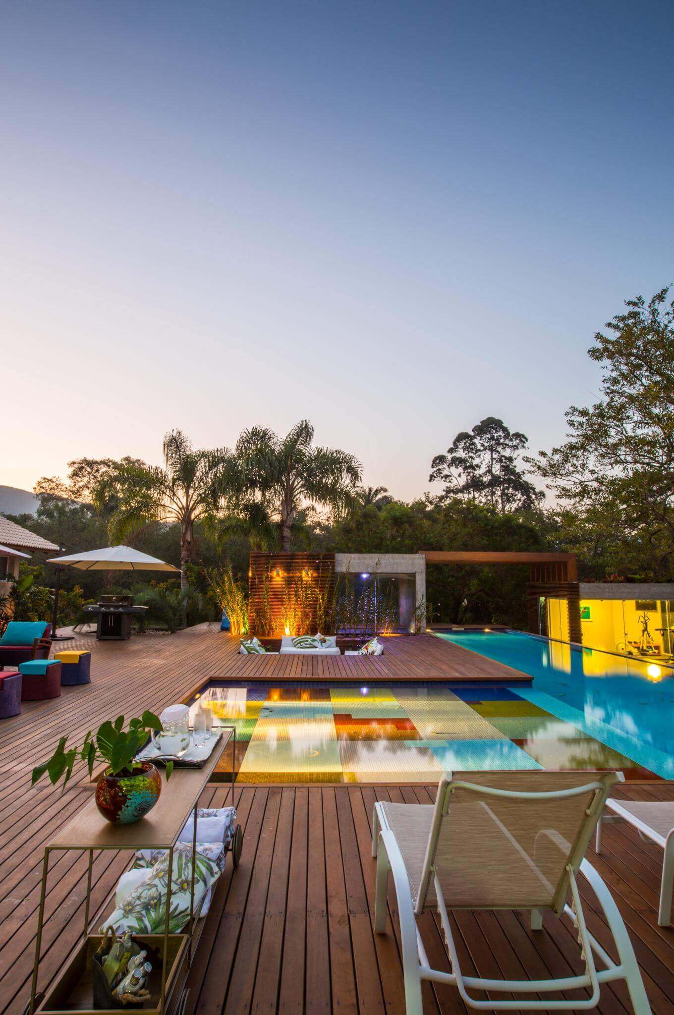 Modern pool area featuring polished wooden decking, vibrant tile designs, tropical landscaping, and inviting evening lighting.