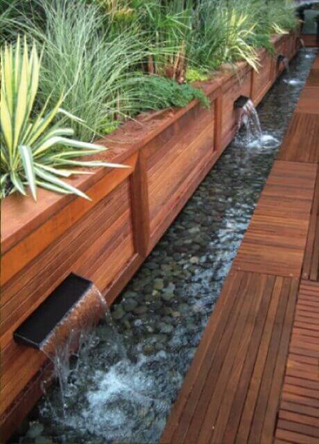 Contemporary wooden deck featuring integrated water elements, lush planters, and a tranquil ambiance, ideal for warm climates.