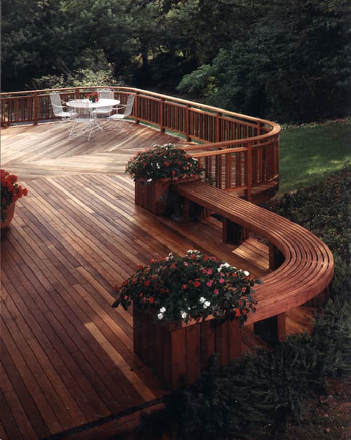 Curved wooden deck with natural finishes, 300 sq ft, featuring built-in planter boxes, circular seating area, and glass table.