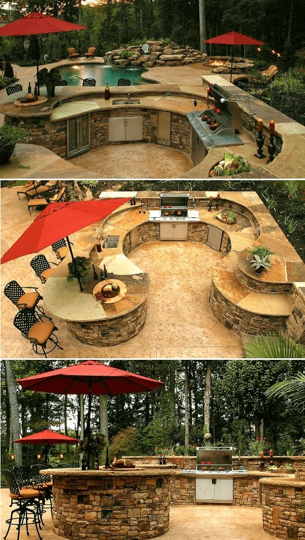 Curved outdoor kitchen with natural stone, grill station, and expansive countertops next to a relaxing pool, shaded by red umbrellas.