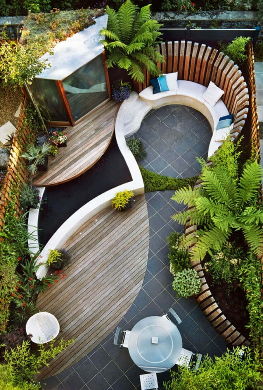 Circular seating in a serene garden features modern outdoor furniture, including a wooden deck, diverse plantings, and a water feature.