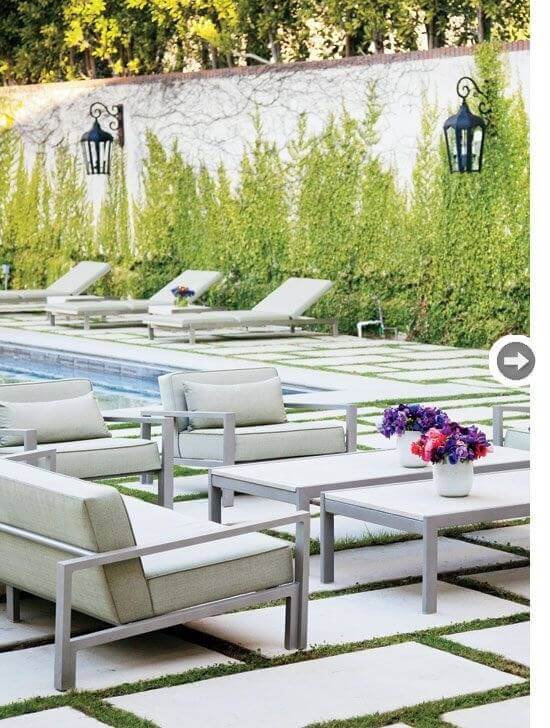 Modern outdoor lounge area with sleek aluminum furniture, light green cushions, and a flower-adorned table on cement pavers surrounded by grass.