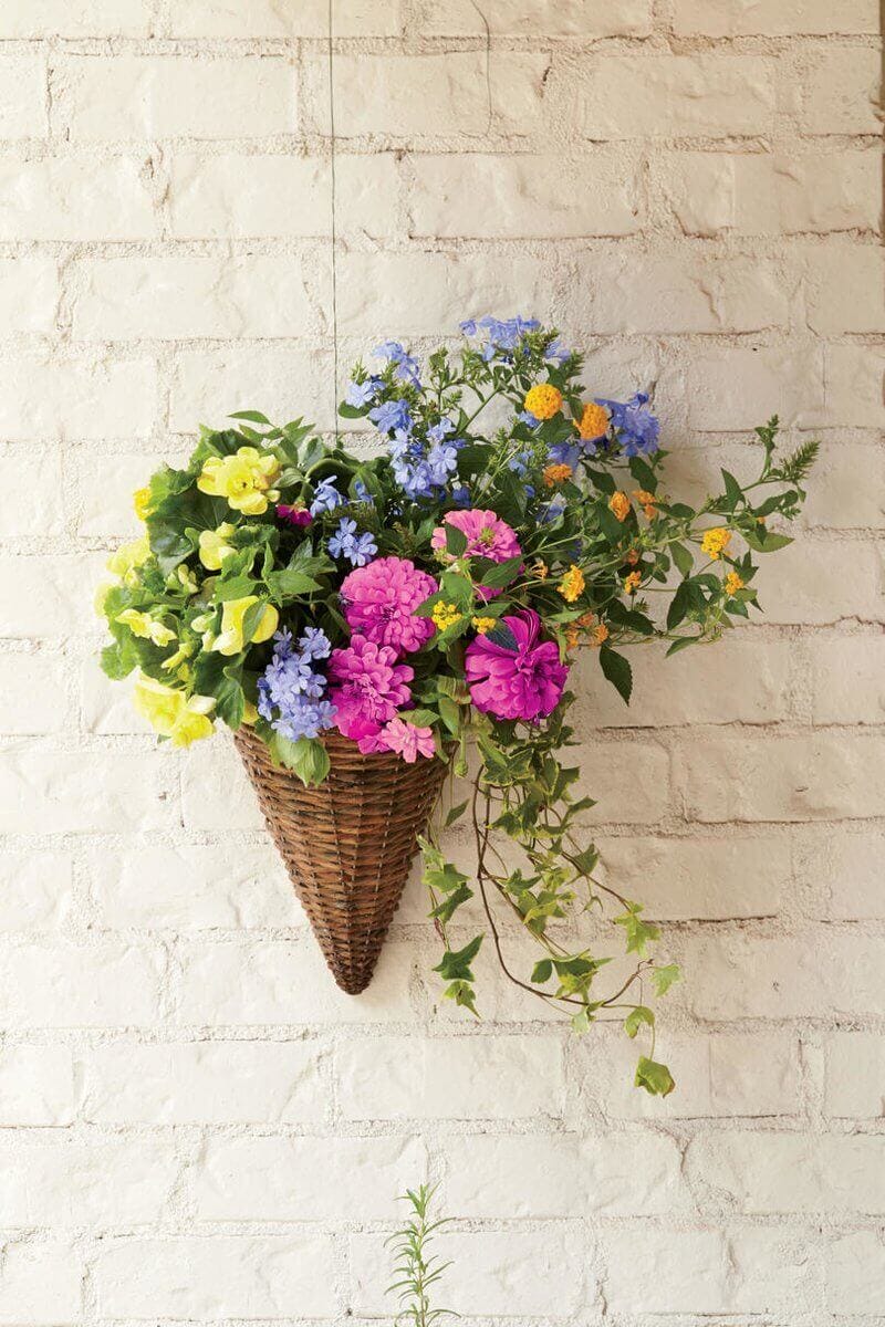 Floral wall art features a cone-shaped basket filled with pink, yellow, and blue flowers, mounted on a white brick wall.