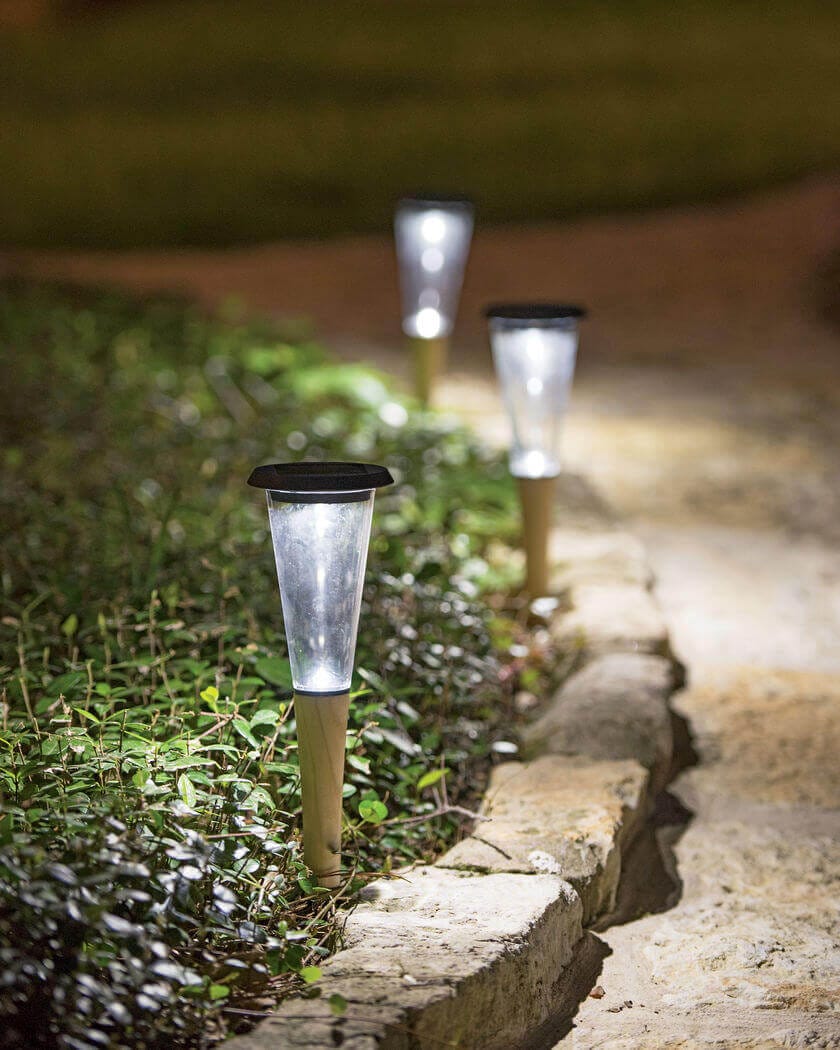 Three solar-powered path lights along a stone pathway, illuminating surrounding plants with soft light, enhancing nighttime visibility.