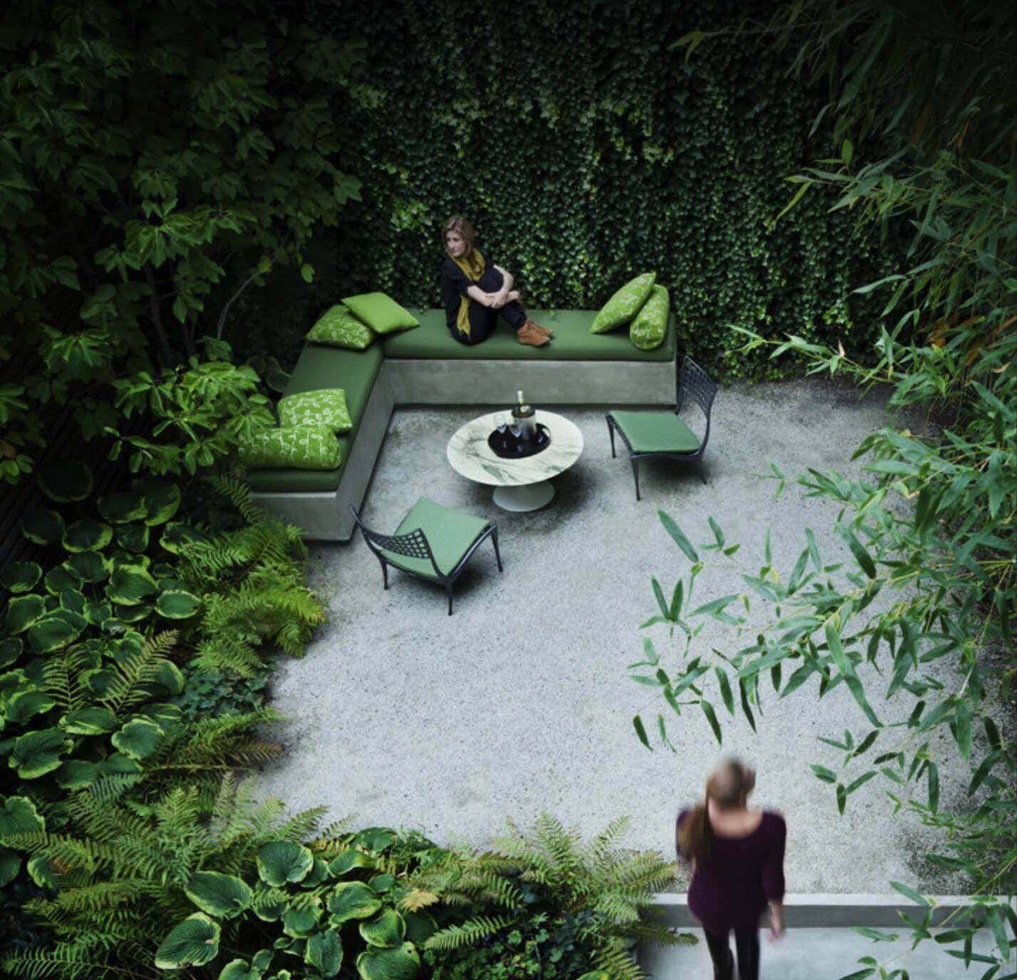 Cozy outdoor living space with an L-shaped concrete bench, green cushions, circular marble coffee table, and lush foliage for a relaxing atmosphere.