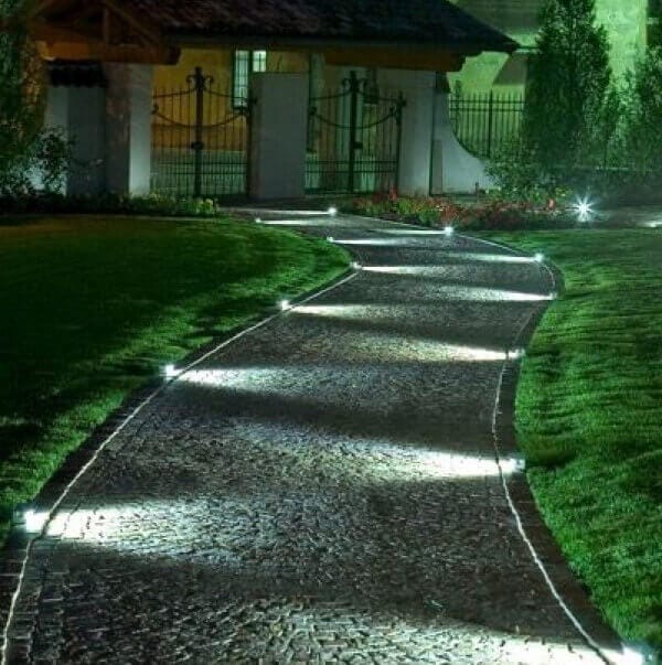 Winding cobblestone pathway illuminated by in-ground LED fixtures, surrounded by grass and shrubs, enhancing nighttime safety and ambiance.