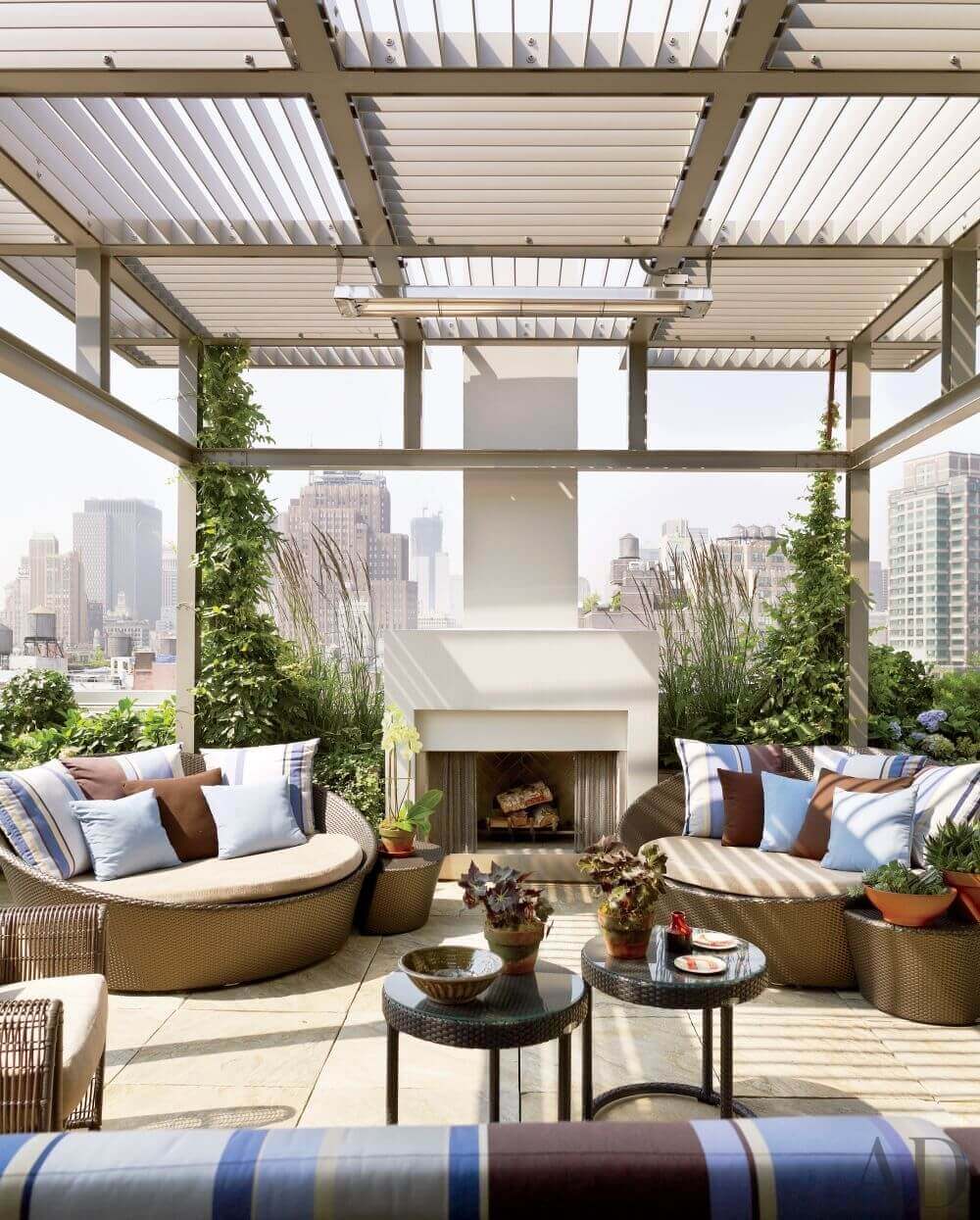 Rooftop garden with curved wicker seating, blue and brown cushions, vertical greenery, and a modern fireplace, shaded by a slatted pergola.