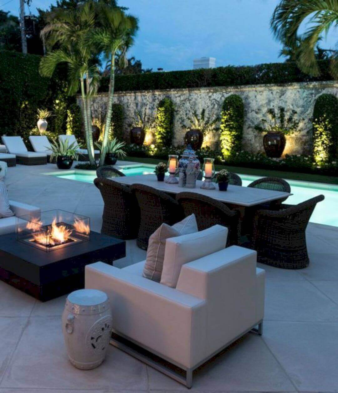 Modern outdoor living space with a swimming pool, white modular seating around a fire pit, and a reclaimed wood dining table for six.
