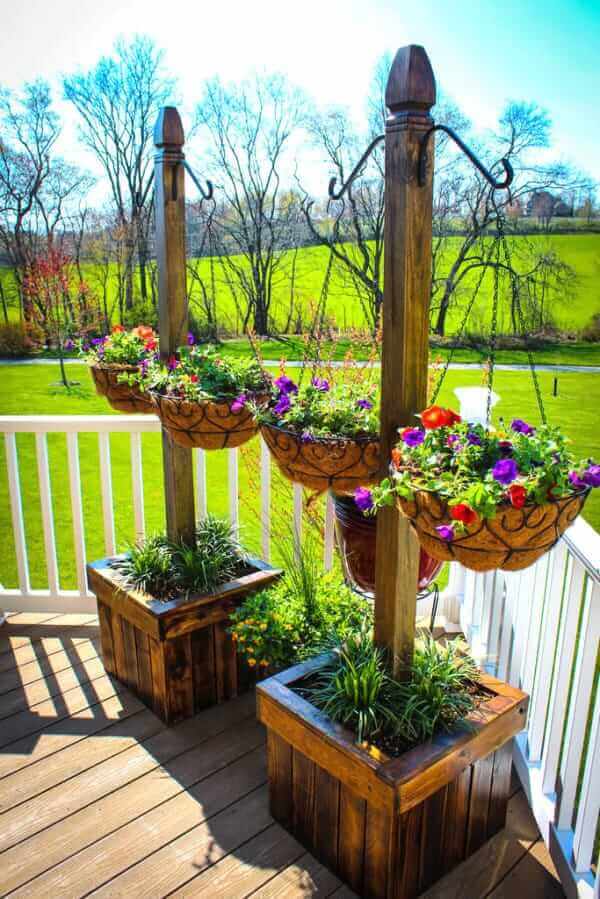 Two vertical wooden planters, about 5 feet high, with four vibrant hanging baskets of pansies and petunias on a sunny deck.