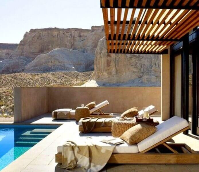 Modern outdoor terrace featuring three reclining lounge chairs of natural wood, a minimalist pool, and a slatted wooden pergola, harmonizing with the desert landscape.