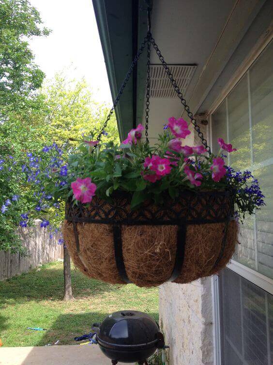 Vibrant hanging basket with pink petunias and blue lobelias, suspended from a metallic chain, enhancing the patio's aesthetic.