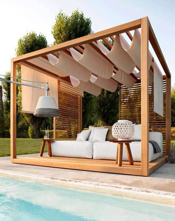 Outdoor lounging pergola with wood frame and sheer fabric drapery, perfect for relaxation by the pool, featuring integrated lighting.