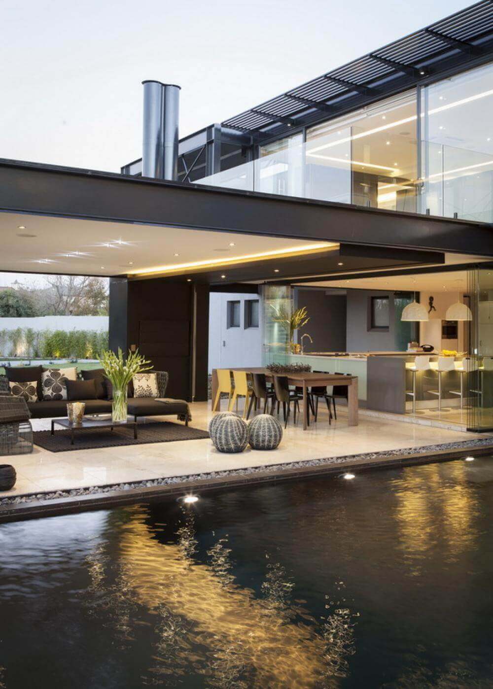 Modern outdoor space featuring a sleek pool, minimalist lounge with chic seating, and a dining area with contemporary chairs, surrounded by greenery.