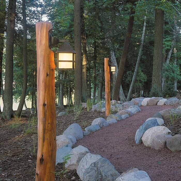 Pathway lit by wooden posts with lanterns, meandering through a shaded forest, enhancing safety and aesthetics along the trail.