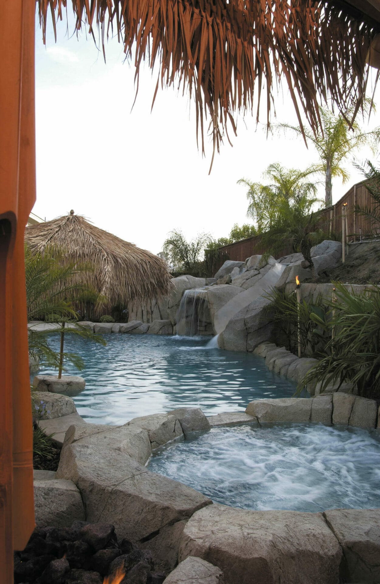 Custom swimming pool features natural stone coping, a waterfall, and tropical landscaping, creating a resort-style atmosphere.