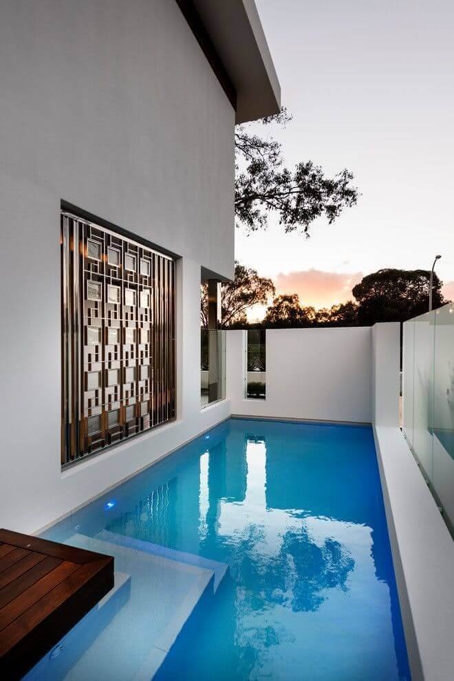 Rectangular swimming pool (3m x 8m) with sleek white walls, glass panels, smooth tile flooring, and a wooden deck for lounging.