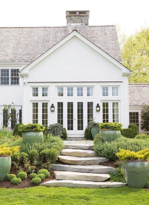 Structured flower bed design with a winding stone pathway, tall rounded planters, and natural stone steps, enhancing curb appeal.