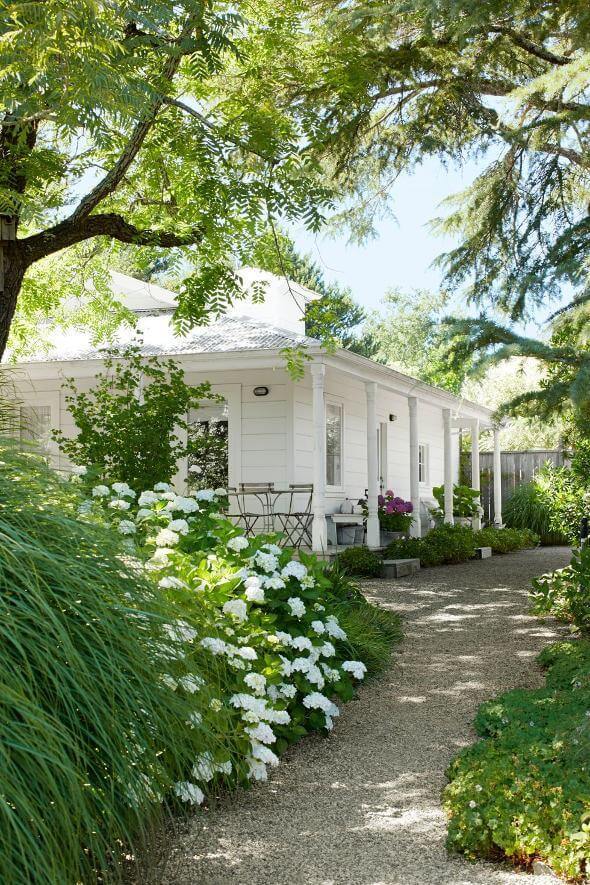 Gravel pathway leads to a house entrance, flanked by lush grasses and white hydrangeas, enhancing curb appeal with a tranquil ambiance.