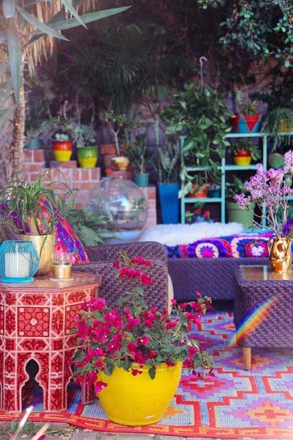 Vibrant bohemian outdoor space with wicker sofas, colorful cushions, a large yellow ceramic planter, and lush greenery, perfect for relaxation.