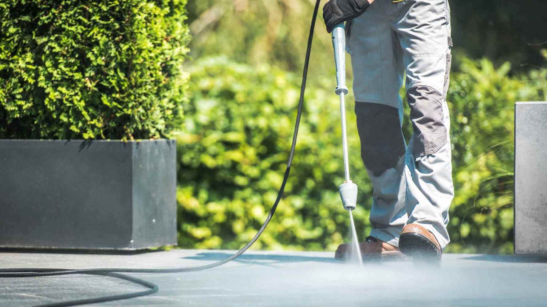 How to clean a concrete patio with a pressure washer. Photo os a person cleaning a concrete patio with a pressure washer.