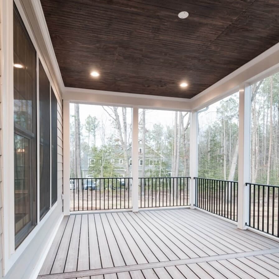 Spacious screened porch designed for outdoor living, featuring wood paneling, composite decking, and unobstructed forest views.