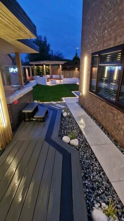 Elegant outdoor living space featuring a grey composite deck, angular pathways, and a gazebo on a raised platform, surrounded by lush grass.