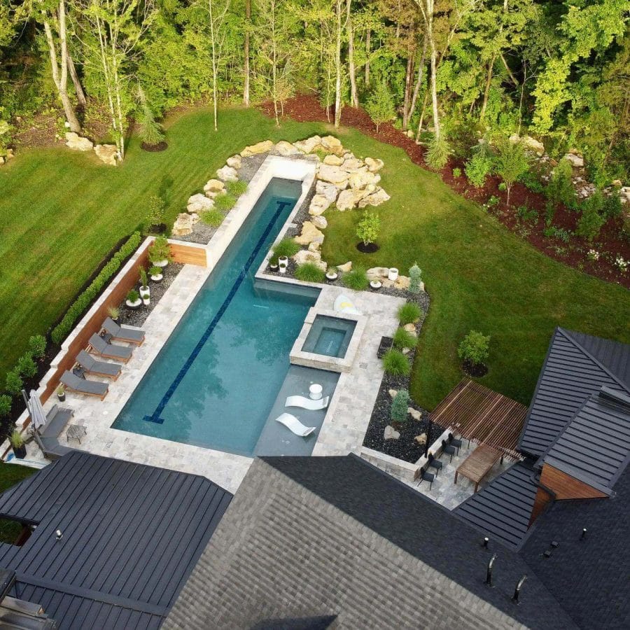Luxurious backyard with an elongated swimming pool, integrated hot tub, sleek deck chairs, and vibrant flower beds, perfect for relaxation.