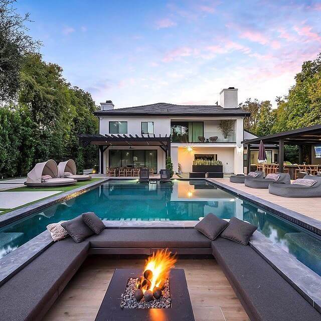 Modern backyard oasis with a sleek rectangular swimming pool, cushioned seating, fire pit, and lush greenery, perfect for relaxation and dining.