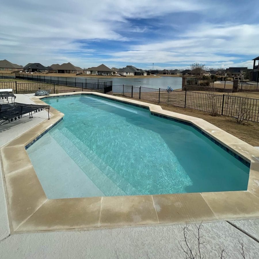 Tranquil backyard with an oval-shaped swimming pool, light concrete patio, and views of distant homes and serene water.