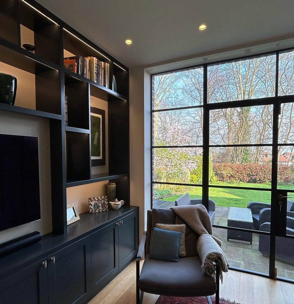 Modern living space with a large glass sliding door, blending indoor and outdoor environments, featuring minimal dark wood shelving and a cozy seating area.