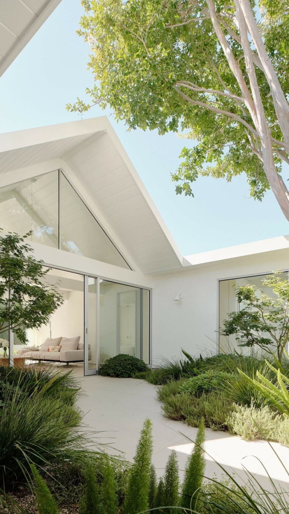 Modern patio design featuring large glass sliding doors that create a seamless indoor-outdoor transition, surrounded by lush greenery.