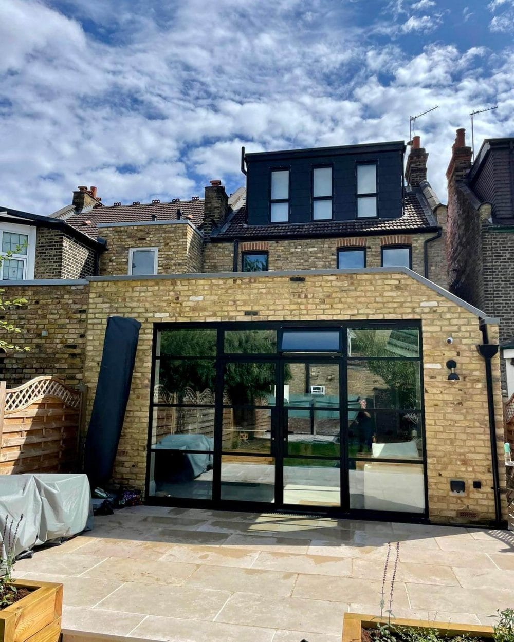 Modern glass extension with large sliding doors, limestone patio, and raised planters. Optimized for sunlight and outdoor interaction.
