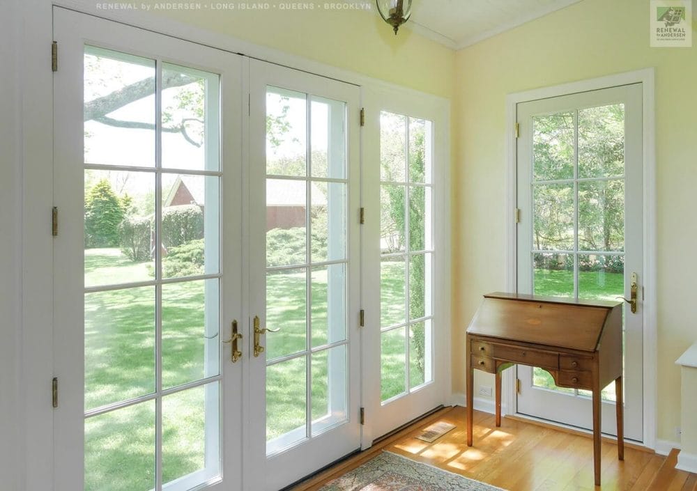 French doors framed in white wood open to a bright interior, enhancing airflow and connecting the indoors to a lush outdoor landscape.