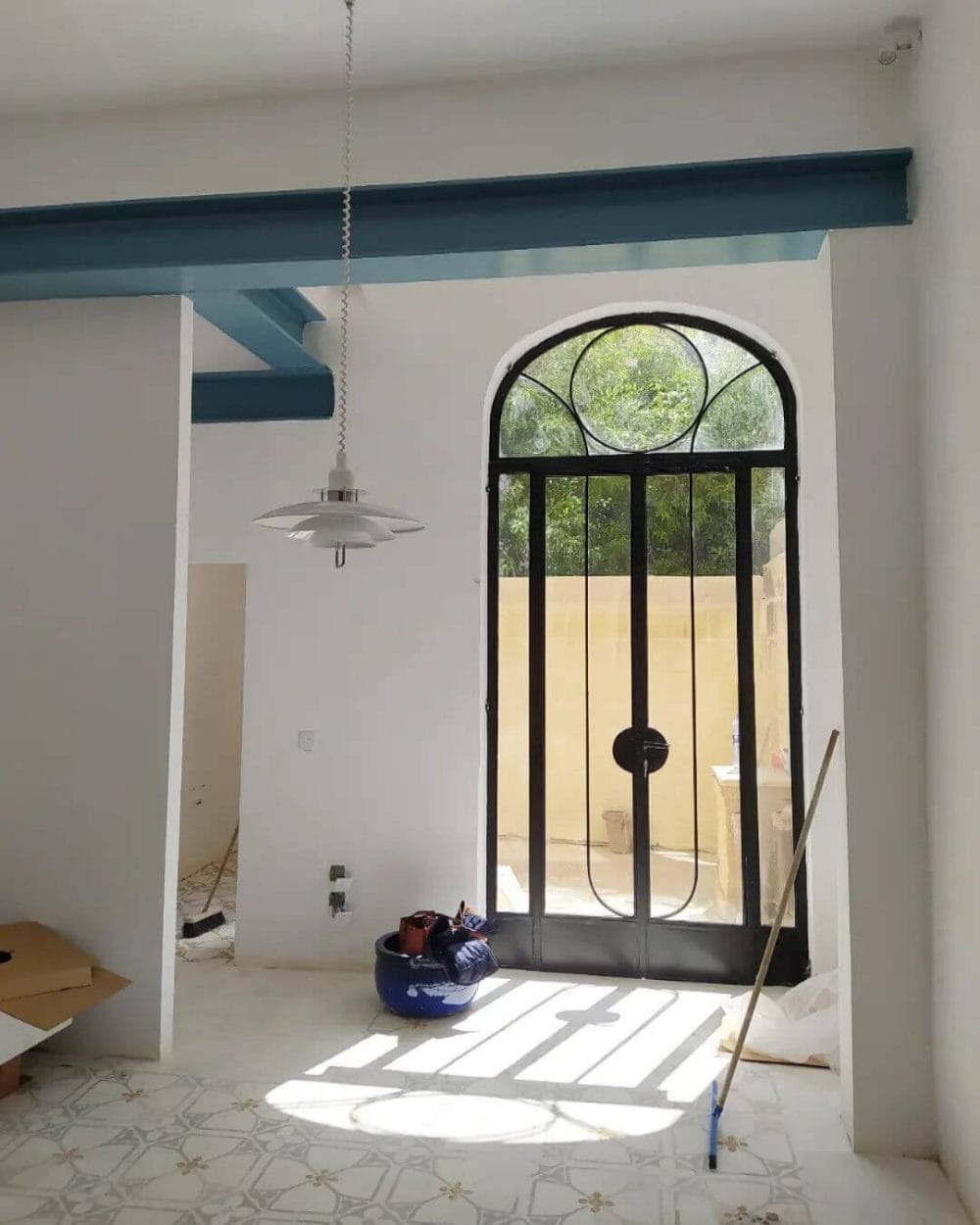 Interior space highlighting an arched black iron entryway door, inviting natural light onto patterned tiles, with a transitional aesthetic.