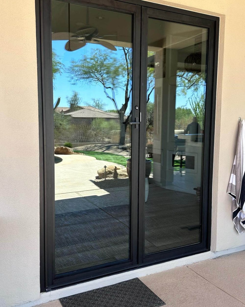 Modern sliding patio door in black aluminum, featuring tempered glass panels, opening to a landscaped yard. Concrete patio with textured surface.
