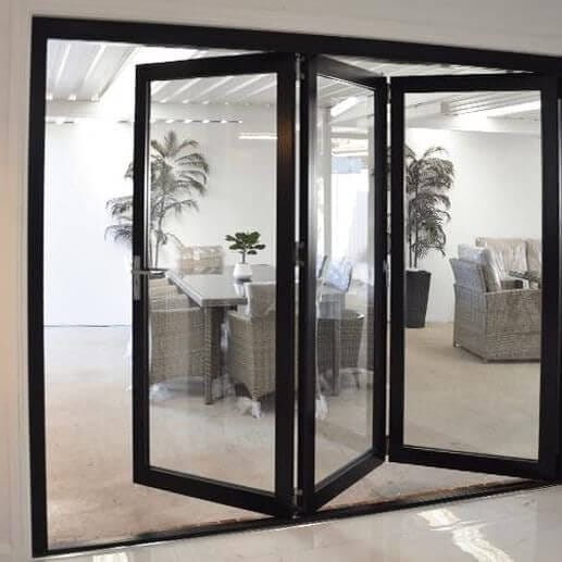 Frameless glass patio doors with black aluminum framing open to a bright dining area, enhancing natural light and modern aesthetics.