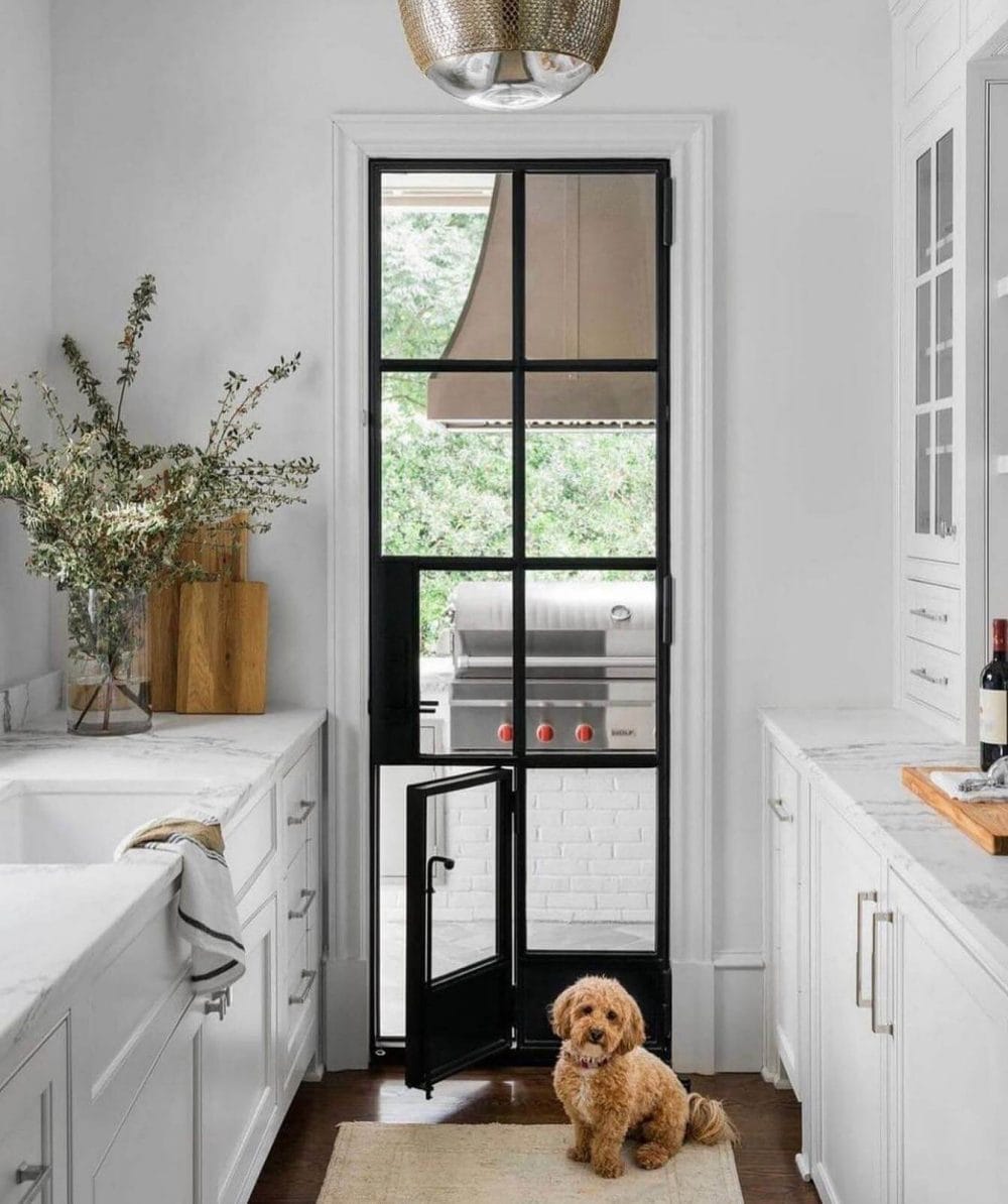 Black-framed glass door leads to a patio with a stainless steel grill, enhancing indoor-outdoor flow in a modern kitchen setting.